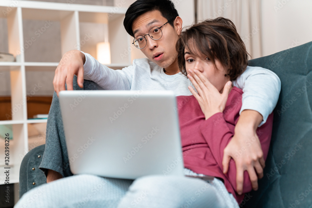 Photo of shocked multinational couple hugging and using laptop Photo of shocked multinational couple hugging and using laptop