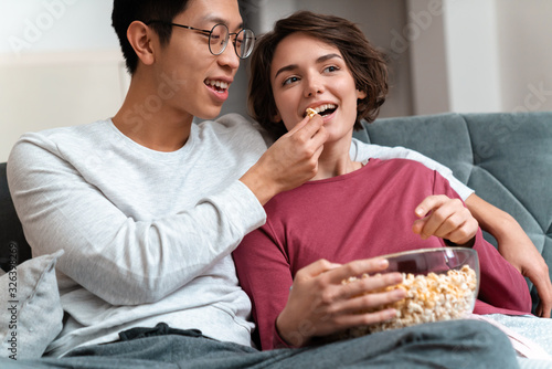 Photo of joyful multinational couple eating popcorn and watching movie