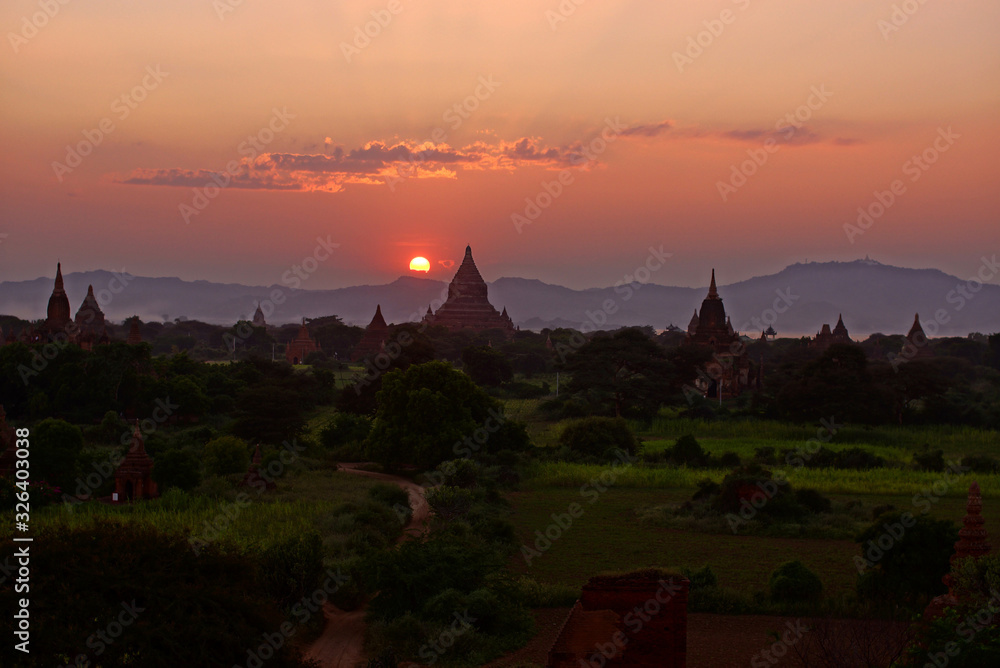 Beautiful sunset over Bagan temples and pagodas in valley, Burma Myanmar. Sun dipping below the horizon and mountains