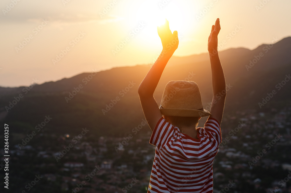 Fototapeta premium Back view, boy raised his hands to meet the sun. Kid on sunset background