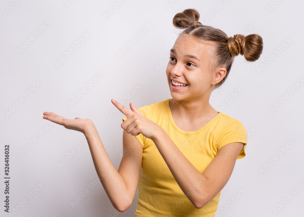 Portrait of teen girl pointing finger away at copyspace, on gray background. Beautiful caucasian young teenager smiling and attracted by attention pointing finger at something. Happy child. Portrait of teen girl pointing finger away at copyspace, on gray background. Beautiful caucasian young teenager smiling and attracted by attention pointing finger at something. Happy child.