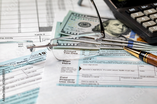 1040 income tax return form 2019 with calculator, money, and pen. Focus through glasses on amount you owe. Concept of filing taxes, payment, refund, and April 15, 2020 tax deadline