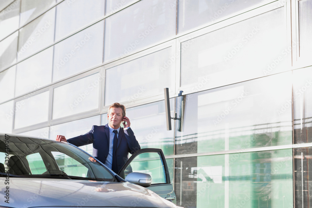 Portrait of mature attractive businessman talking on smartphone while standing outside the car Portrait of mature attractive businessman talking on smartphone while standing outside the car