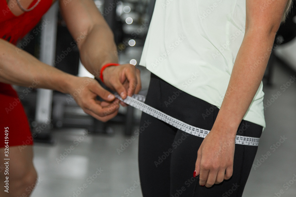 weight loss, personal trainer, nutritionist, fitness, motivation, healthy lifestyle. a man measures a girl's hips with a tape measure. Close up, macro photo. Preparation for training.