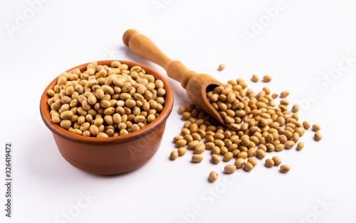 Soyabeans in brown plate and wooden spoon, scattered on white background