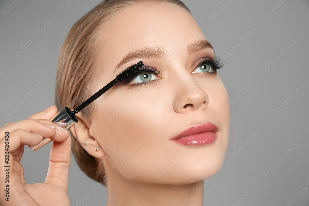 Beautiful woman applying mascara on light grey background. Stylish makeup
