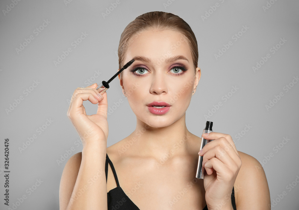 Fototapeta premium Beautiful woman applying mascara on light grey background. Stylish makeup