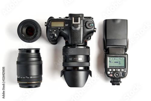 top view of modern digital camera equipment - DSLR with attached zoom lens and hood, lenses and external flashlight on white background photo