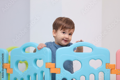 Cute little child playing in modern playpen at home photo