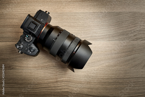 top view of a modern digital mirrorless full-frame camera with attached zoom lens and hood on wooden table