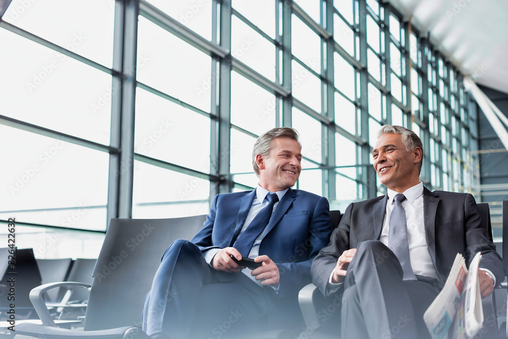 Mature businessmen talking while sitting and waiting for boarding in airport Mature businessmen talking while sitting and waiting for boarding in airport
