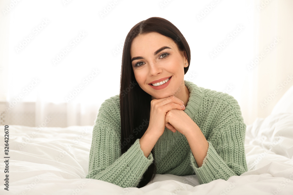 Young woman wearing warm sweater on bed at home. Winter season Young woman wearing warm sweater on bed at home. Winter season