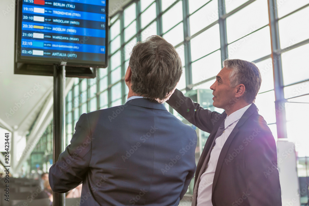 Portrait of mature businessmen looking at their flight on monitor in airport Portrait of mature businessmen looking at their flight on monitor in airport