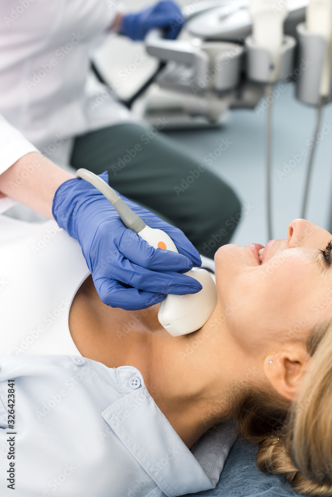 Fototapeta premium doctor examining thyroid of smiling woman with ultrasound scan in clinic