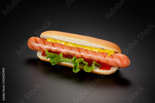 Hot dog with ketchup, mustard and green lettuce on a black background.