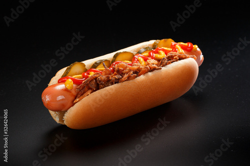 Danish hot dog with pickled cucumbers, fried onions and a hot dog with mustard, lettuce and jalapenos on a black background. photo