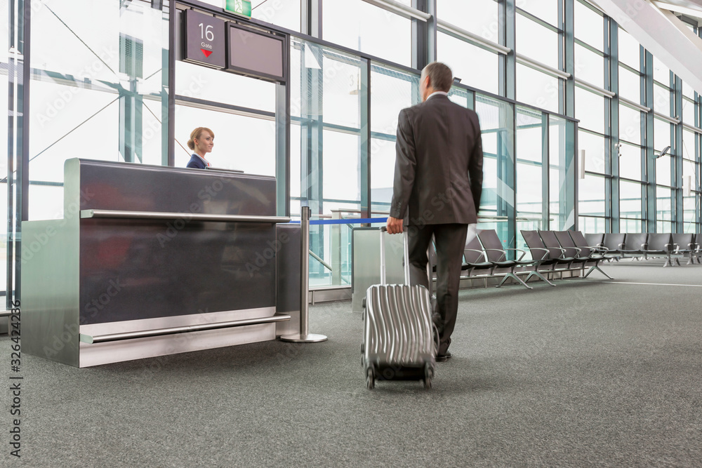 Φωτογραφία Rear view of mature businessman walking with his suitcase on his gate for boardi