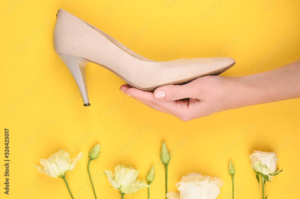 The concept of womens shoes. Womens beige shoes on a hand in flowers. on a yellow background. beige shoes on the hand for girls. Wallpaper and flowers. Place for writing