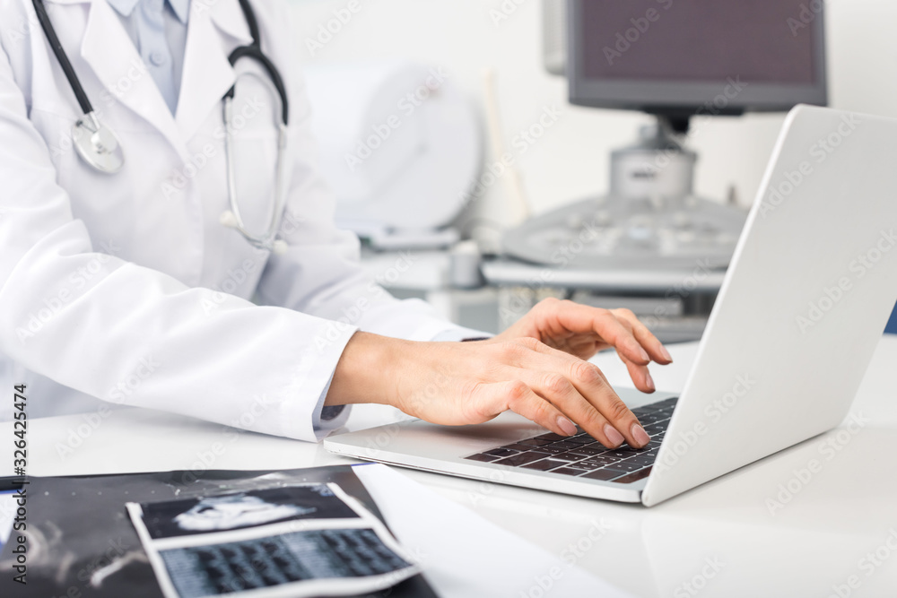 cropped view of doctor working on laptop with ultrasound scans on table cropped view of doctor working on laptop with ultrasound scans on table