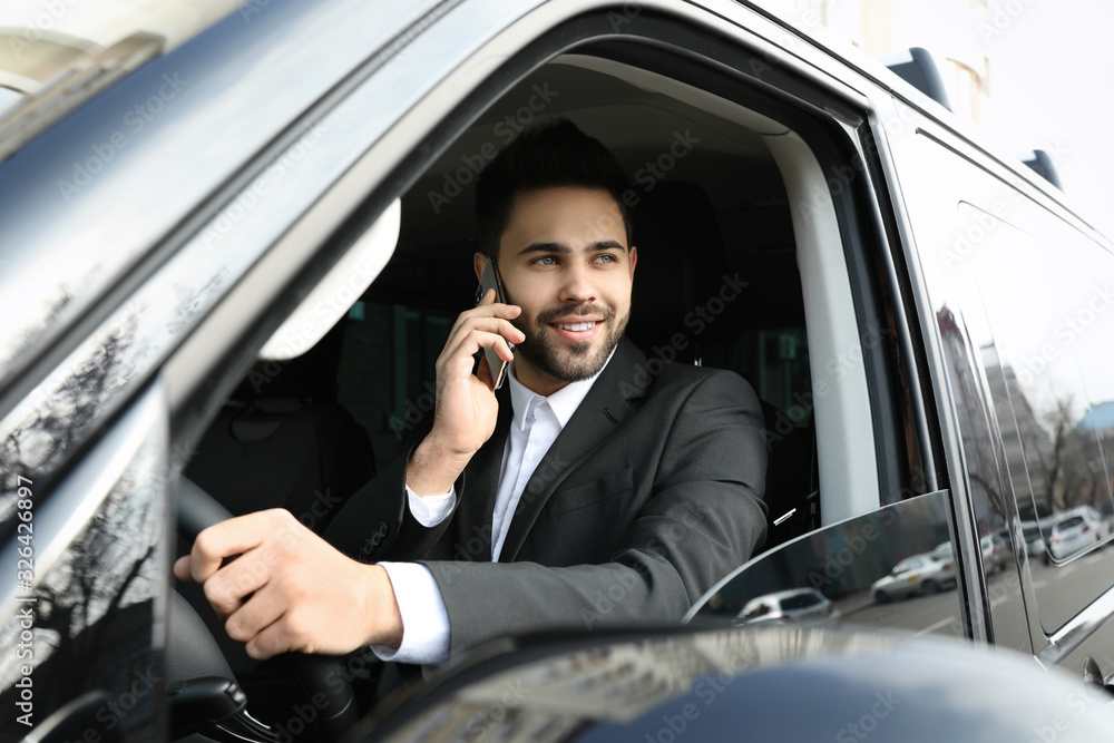 Handsome young man talking on smartphone while driving his car Handsome young man talking on smartphone while driving his car