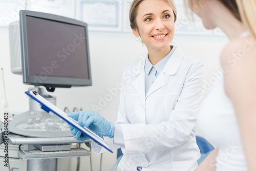 smiling doctor showing diagnosis to patient in clinic near ultrasound scanner