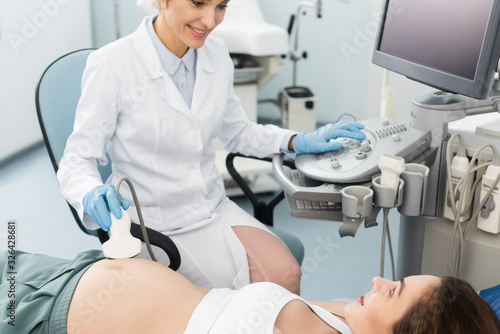 professional doctor examining belly of pregnant woman with ultrasound scan in clinic