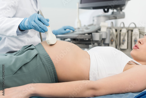 cropped view of doctor examining belly of pregnant woman with ultrasound scan in clinic