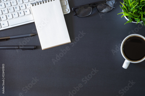 Workplace office with dark black desk. Top view from above of keyboard with notepad and coffee cup. Space for modern creative work of designer. Flat lay with copy space. Business and finance concept.