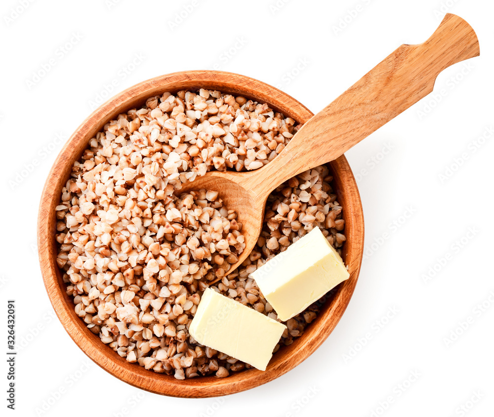 Boiled buckwheat in a wooden plate with a spoon and pieces of butter on a white. The view from the top Boiled buckwheat in a wooden plate with a spoon and pieces of butter on a white. The view from the top