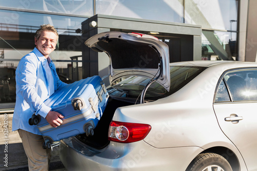 Portrait of mature businessman putting his luggage on car trunk with lens flare