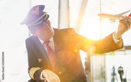 Portrait of mature pilot holding airplane toy while playing with cute little girl in airport photo