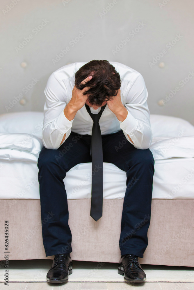 Fototapeta premium Stressed and overworked businessman sitting on the bed