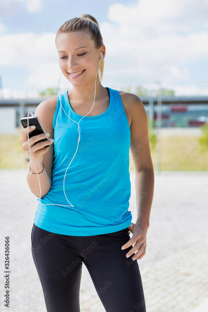 Portrait of young attractive woman standing while using and listening to music on her smartphone in park Portrait of young attractive woman standing while using and listening to music on her smartphone in park