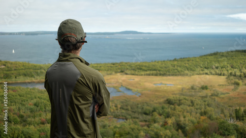 Adult man on a hike looking out over a vast forested landscape with valley, river and ocean © gage