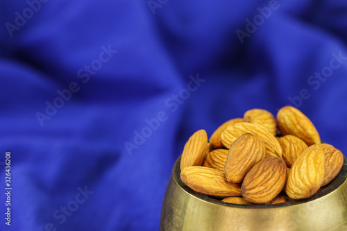 Almonds in a brass bowl on a blue background