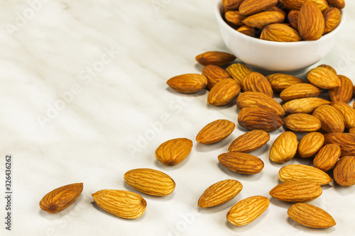 Almonds lie on a white marble surface and in a white bowl