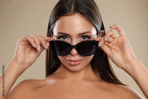 Beautiful young woman wearing sunglasses on beige background