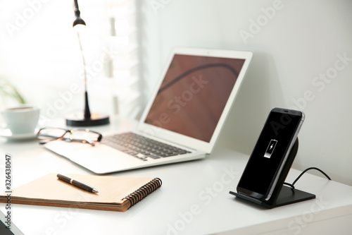 Mobile phone with wireless charger on white table. Modern workplace accessory