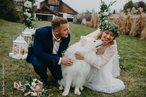 Bilde på lerret Newlyweds play with dog on background of lawn and house.
