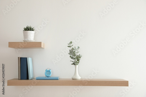 Wooden shelves with beautiful plants  alarm clock and books on light wall