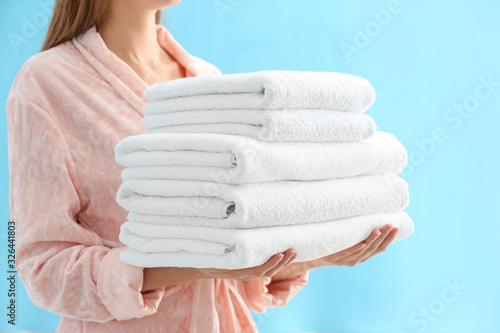 Woman holding stack of fresh clean towels on light blue background, closeup