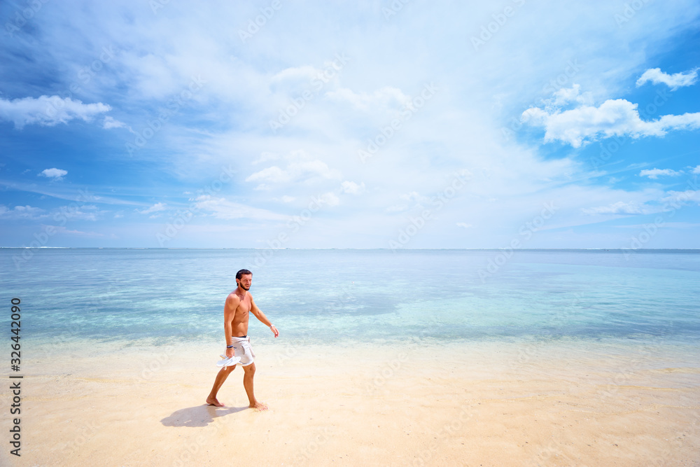 Tropical vacation. Young man walking by beautiful white sand sea beach.