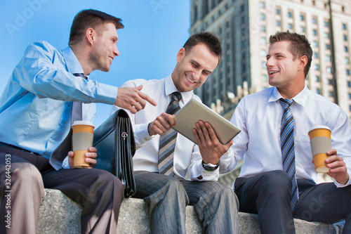 Fototapeta Naklejka Na Ścianę i Meble -  Portrait of handsome businessman showing business plan to the other businessman over digital tablet while sitting