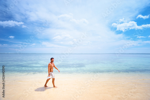 Tropical vacation. Young man walking by beautiful white sand sea beach.