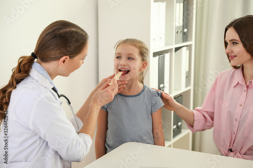 Mother and daughter visiting pediatrician. Doctor examining little patient's throat in hospital