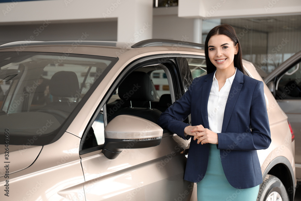 Young saleswoman near new car in dealership