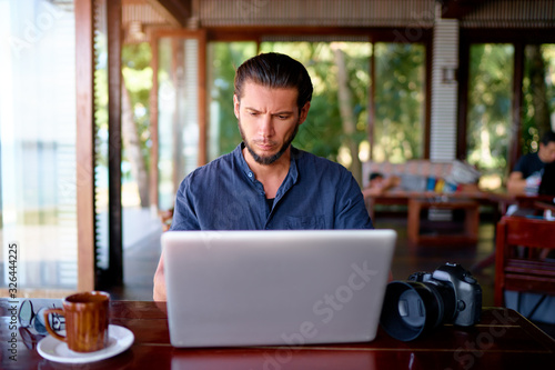 Freelance concept. Young bearded man working on laptop computer while sitting on cafe terrace.