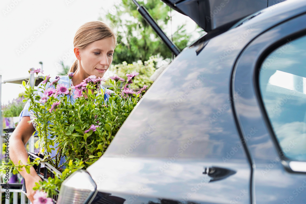 Portrait of mature female gardener putting flowers on car trunk for delivery - obrazy, fototapety, plakaty 