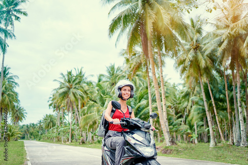 Tropical travel and transport. Happy young woman in helmet riding scooter on the road with palm trees.