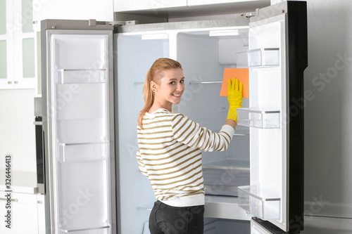 Woman in rubber gloves cleaning empty refrigerator at home